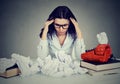 Too much work stressed woman sitting at her disorganized desk with books and many paper balls