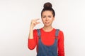 Too small! Portrait of dissatisfied girl with hair bun in denim overalls showing a little bit gesture and looking disappointed