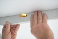 Tool level in men's hands and a flat horizontal surface of the ceiling. Styrofoam, seiling mounting. Royalty Free Stock Photo