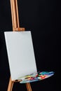 Tools of the artist. Brushes, wooden easel tripod, palette colorful. Black background, studio, nobody. Royalty Free Stock Photo