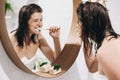 Tooth care concept. Young happy woman in white towel brushing teeth and looking at round mirror in stylish bathroom. Slim Royalty Free Stock Photo