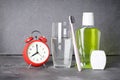 Dental and morning concept. Toothbrush, mouthwash, dental floss, glass of water and alarm clock on a gray background Royalty Free Stock Photo