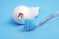 Toothbrush with toothpaste on it and white toothpaste tube on blue background