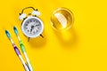 Toothbrushes, glass of water with lemon and alarm clock on a yellow background