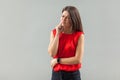 Toothy ache. Portrait of upset brunette young woman in red shirt standing, touching her cheek because feeling pain on her teeth Royalty Free Stock Photo