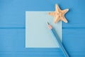 Top above overhead view close-up photo of a blank note with a small starfish and a pencil isolated on blue wooden background with Royalty Free Stock Photo