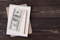 Top above overhead view flat lay photo of blank notebook pencil and a stack of dollars isolated on wooden background with Royalty Free Stock Photo
