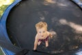 Top above view of cute little caucasian funny blond toddler boy stand inside big black trampoline at home backyard