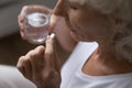 Retired woman holding pill and glass of water.