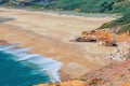 Top aerial view of sandy beach with rocks and cliffs and waves of azure turquoise water of Atlantic Ocean near Nazare town