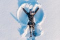 Top aerial view of young happy smiling girl making by arms snow angel figure and lying in snow, winter outdoor activity