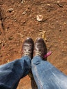 Top angle view of men leg in Blue color jeans with old damaged brown color shoes on stony clay ground on background. Picture Royalty Free Stock Photo