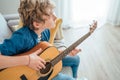 Top angle view at Preteen boy playing acoustic guitar dressed casual jeans, blue shirt sitting on the cozy sofa at the home living Royalty Free Stock Photo