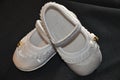 On top of a black cloth, a pair of white baby shoes, with gold detail on the side, ruffles around the entire shoe, with elastic Royalty Free Stock Photo