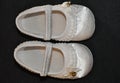 On top of a black cloth, a pair of white baby shoes, with gold detail on the side, ruffles around the entire shoe, with elastic Royalty Free Stock Photo