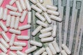 Top close up shot of white pills scattered on top of a few hundreed dollar bills. Pink background. Healthcare, medical, Royalty Free Stock Photo