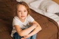 Top close-up view of distraught beautiful little girl with wet eyes from tears sits on bed in bedroom and looking at Royalty Free Stock Photo