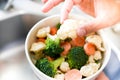 Top close up view of mixed fresh raw vegetables in white ceramic bowl in a house kitchen with hand holding cauliflower Royalty Free Stock Photo