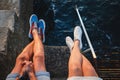 Top close up view of young couple legs in sneakers sitting on pier near to the sea, travel concept Royalty Free Stock Photo