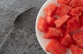 Top close view of a plate of watermelon chunks with a fork on a gray mottled table