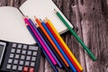 Top closeup of a notebook with a pack of colored pencils and a black calculator, wooden background Royalty Free Stock Photo