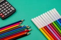 Top closeup of a pack of colored pencils, marker pens, and a black calculator on green background Royalty Free Stock Photo