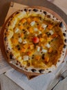 Top closeup of pizza with vegetables on a wooden board, newspapers around