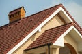 Top detail of big modern expensive residential cottage with steep shingled roof, brick chimney, stucco walls on blue sky