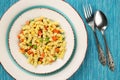 Top down, flat lay of delicious, vegetarian fusilli pasta with basil pesto, sweet corn, carrot and peas in a plate on a turquoise Royalty Free Stock Photo