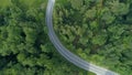 TOP DOWN: Flying above an empty asphalt road winding past forests and meadows.