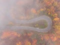 TOP DOWN: Flying above a hairpin turn of a scenic forest road on foggy fall day. Royalty Free Stock Photo
