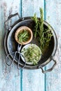 Top down vertical view of herbs in bowls in a metal tray with scissors, against a blue wooden background.