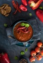 A top down view of a bowl of roasted red pepper soup topped with roasted red peppers and basil ready for eating.