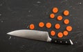 Top down view, chefs knife and small circles of sliced carrot on black marble like working board Royalty Free Stock Photo