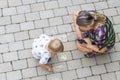 Top-down view on child drawing on paving slabs and woman watching him.