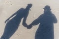 The top down view of a familys shadows on the beach sand. A man in a hat is holding hands with a woman in a bikini and cap