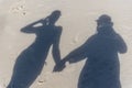 The top down view of a familys shadows on the beach sand. A man in a hat is holding hands with a woman in a bikini and cap