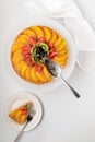Top down view of German fruit flan on a white cake stand with one slice on a plate on the side.