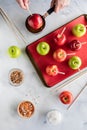 Top down view of hands dipping an apple into caramel sauce surrounded by ingredients to make caramel apples. Royalty Free Stock Photo