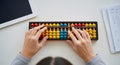 Top-down view of hands operating a colorful abacus on a white desk, with a tablet Royalty Free Stock Photo