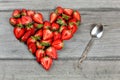 Top down view, heart made from strawberry pieces, silver spoon next to it, on gray wood desk