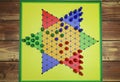 Top down view on isolated yellow gamboard with hexagon, multicolored game pieces, wooden background - chinese checkers sternhalma