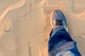 Top down view of man extending a foot with a worn sneaker jeans on dusty sand showing travel and trekking during evening