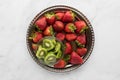 A top down view of a metal tray of strawberries and a small bowl of sliced kiwis. A complimentary colour concept.