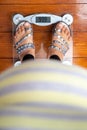 Top down view of an obese women wearing sandals standing on top of a weighing scale