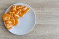 Top down view of pealed mandarin peaces on white plate, wooden desk surface