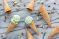 A top down view of pistachio ice cream cones with several empty cones on a marble slab.