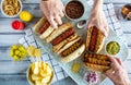 A top down view of a platter of gourmet hotdogs with hands helping themselves to a hotdog.