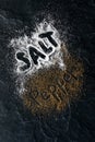 Top down view of salt and pepper scattered on black slate board with the words salt and pepper printed inside. Royalty Free Stock Photo