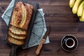 A top down view of a sliced banana loaf on a wooden board with a cup of coffee against a dark wooden background. Royalty Free Stock Photo